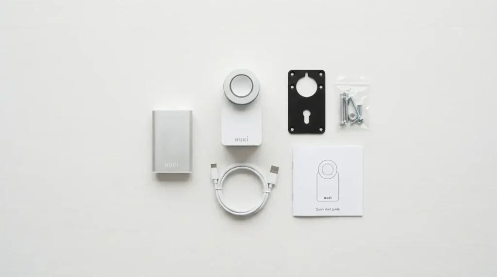 nuki-smart-lock-pro-whats-in-the-box Nuki Smart Lock Pro Review UK — what's in the box: smart lock, Power Pack rechargeable battery, USB-C cable, mounting plate, screws, and quick start guide on white table